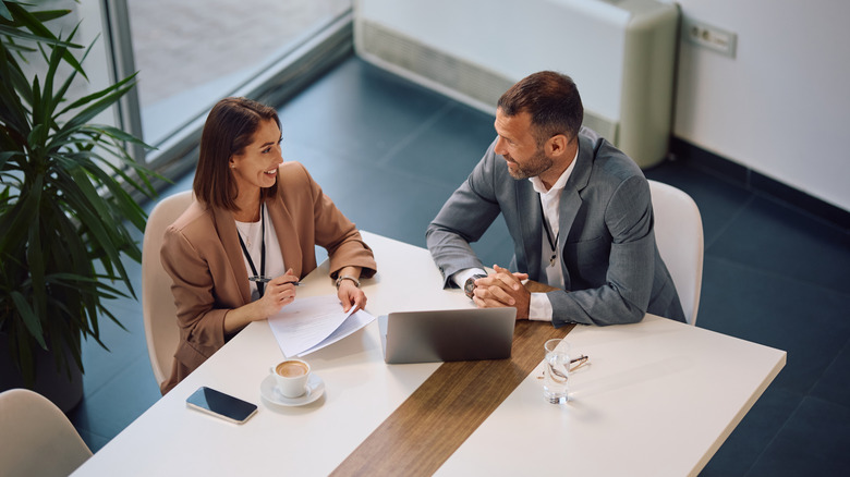 High angle view of happy entrepreneur and her colleague talking during business meeting in the office.