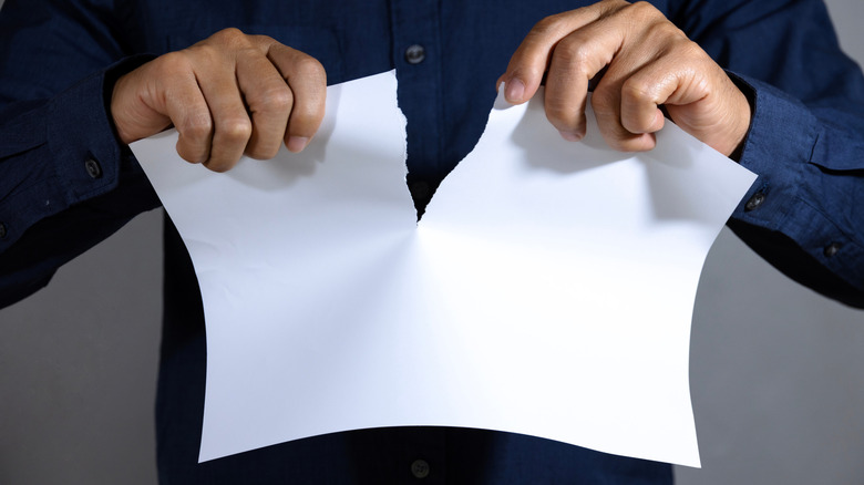 Man tearing blank white paper into two parts.
