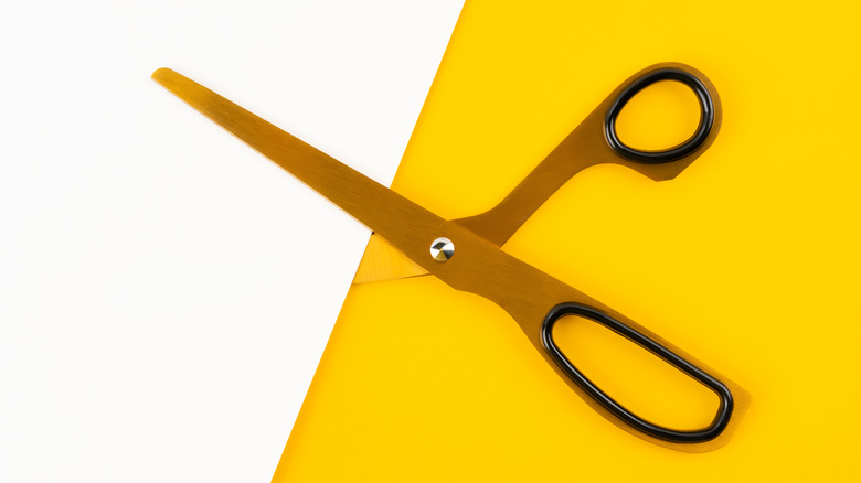Scissors cutting white paper on yellow background.
