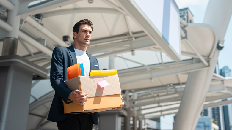 Frustrated man holding box of office supplies after being fired.