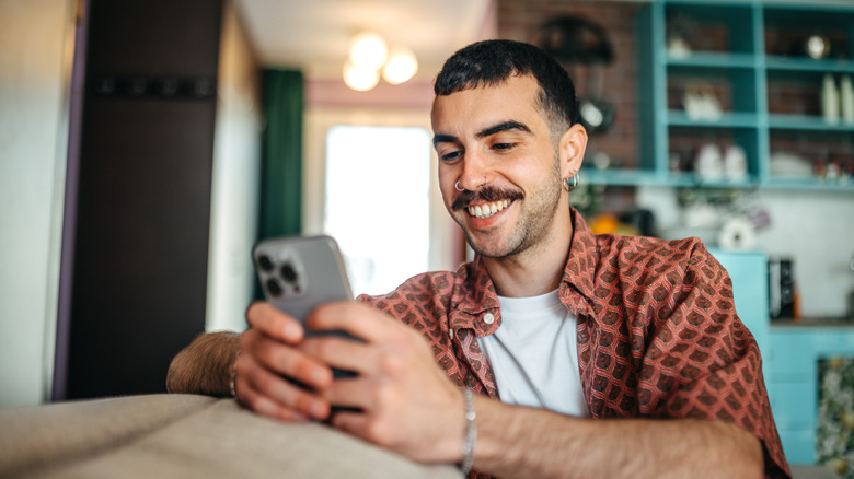 Cheerful young man using smart phone while relaxing on a sofa at home.