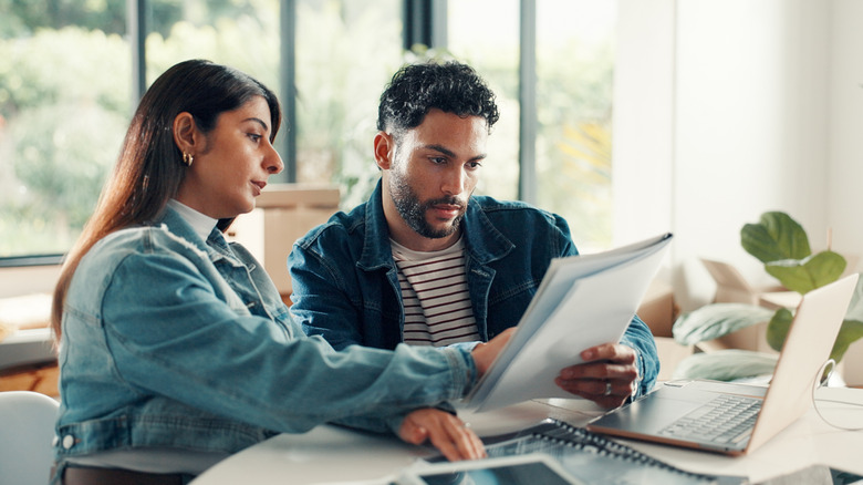 Couple looking at papers in front of laptop.