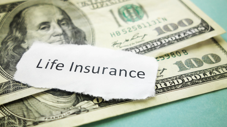 A paper scrap with LIFE INSURANCE written on it on top of two one hundred dollar bills.