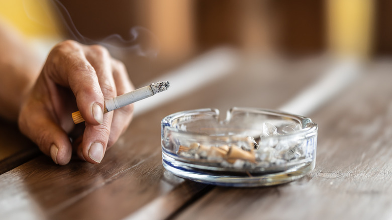 The hand of a smoking woman with a cigarette taps the ash into an ashtray.
