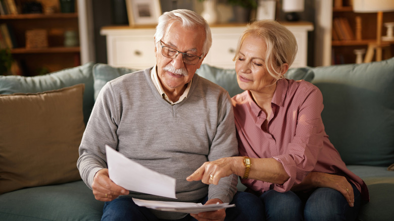 A senior couple reading documents together on a couch.