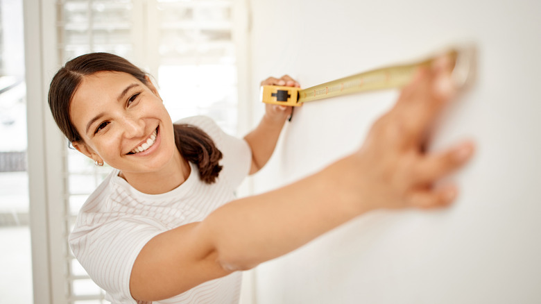 Smiling woman uses tape measure to examine a wall
