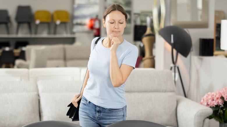 A young woman with her hand on her chin examining furniture on display