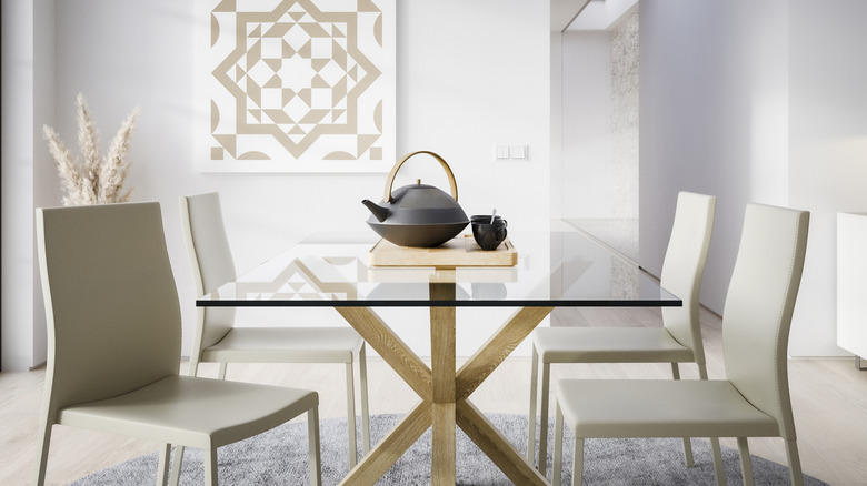 A glass table with a wooden frame topped by a modern tea set and surrouded by simple white chairs