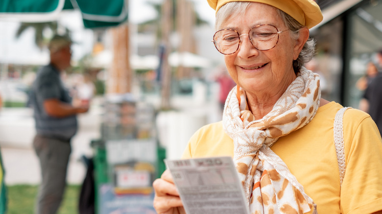 Smiling old woman checks if the lottery ticket was lucky.