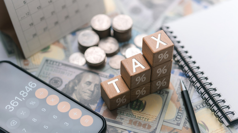 Blocks arranged like steps spell "tax" while surrounded by calendar, coins, cash, and calculator