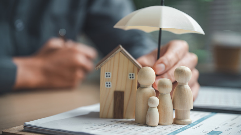 Wooden house and figures under an umbrella held by a human hand