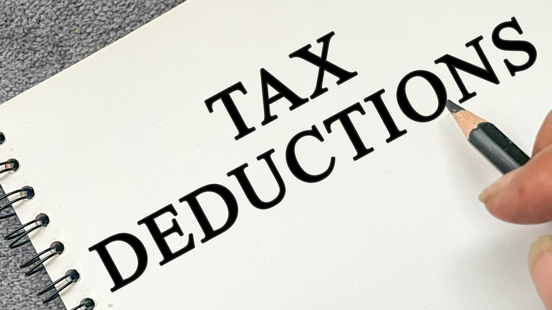A person holds a pencil over a notebook with tax deductions written on the top page