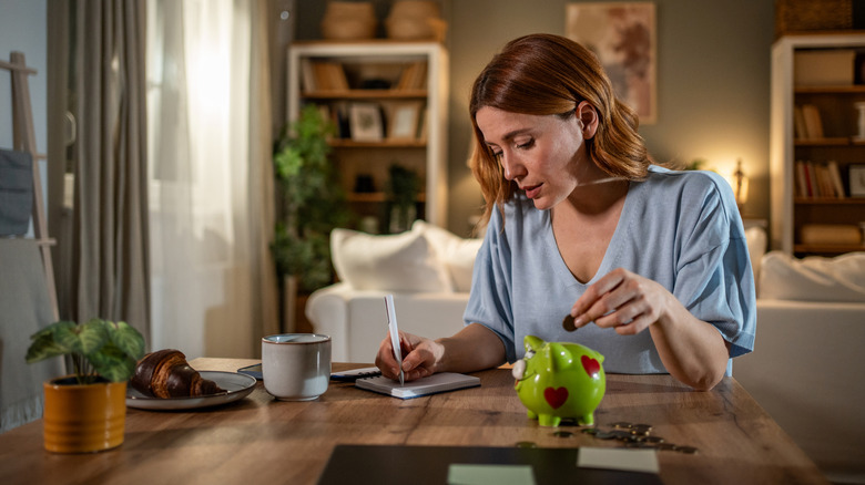 Women doing calculations while putting money in a piggy bank.