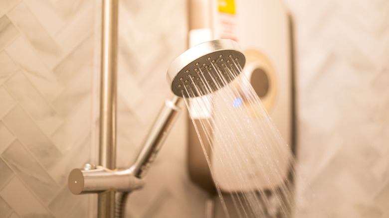 A cheery little shower head sprays water in a warmly-lit shower stall.