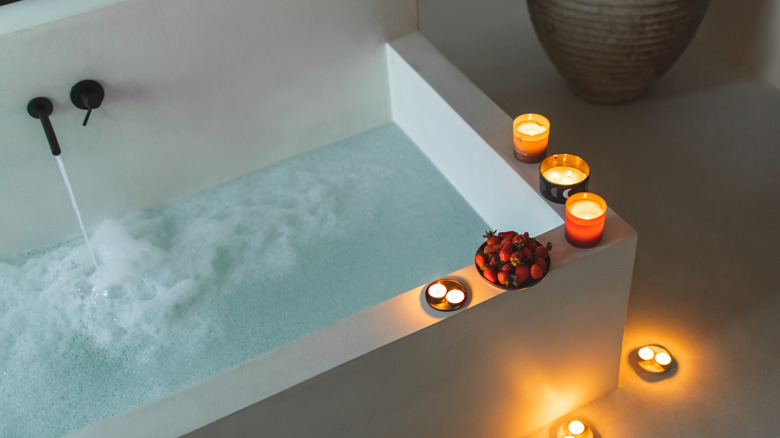 An inviting half-full bath in a modern tub, surrounded by candles.