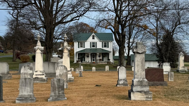 Gravestones arranged on a dried up cemetery field with the front of a house in the background
