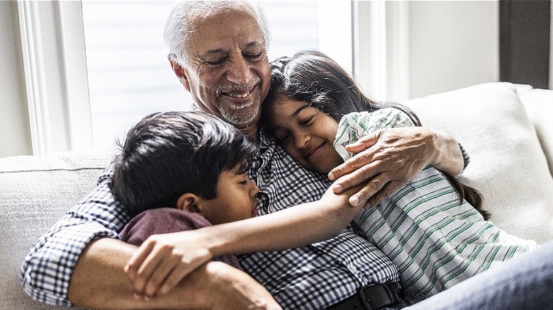 Older person smiling, hugging grandkids