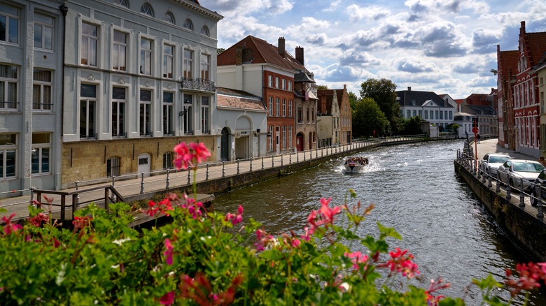 Belgium village with flowers in the foreground and boat filled with people coming up river in background