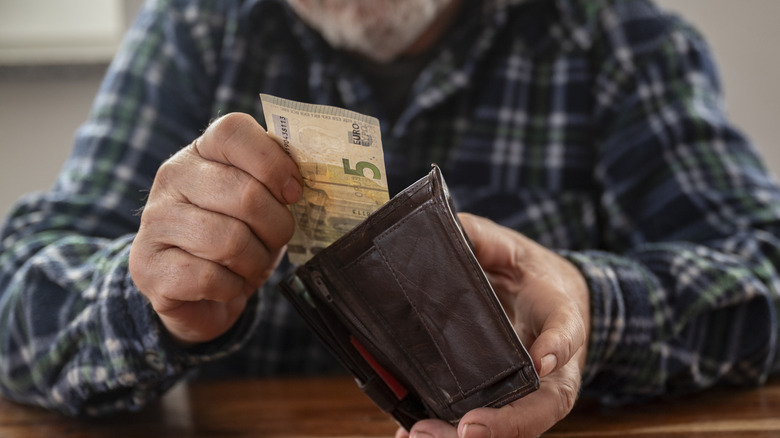 Seated old man pulls five dollar euro out of wallet