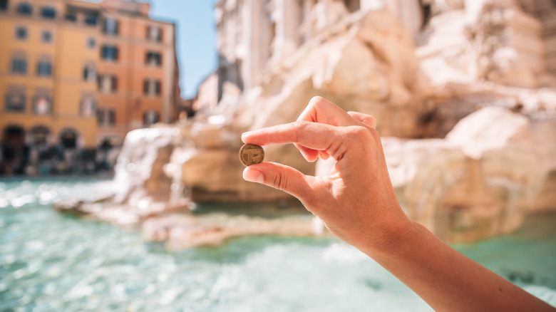 Woman's hand holding a coin at the Trevi Fountain in Rome, Italy.