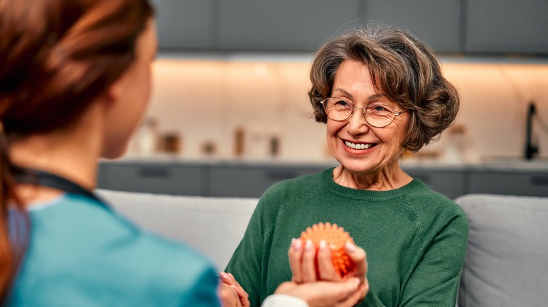 An active senior woman smiles at her physical therapist while squeezing a spiked therapy ball