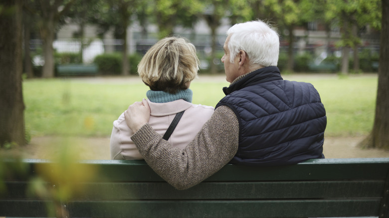 Senior couple on green park bench with backs turned