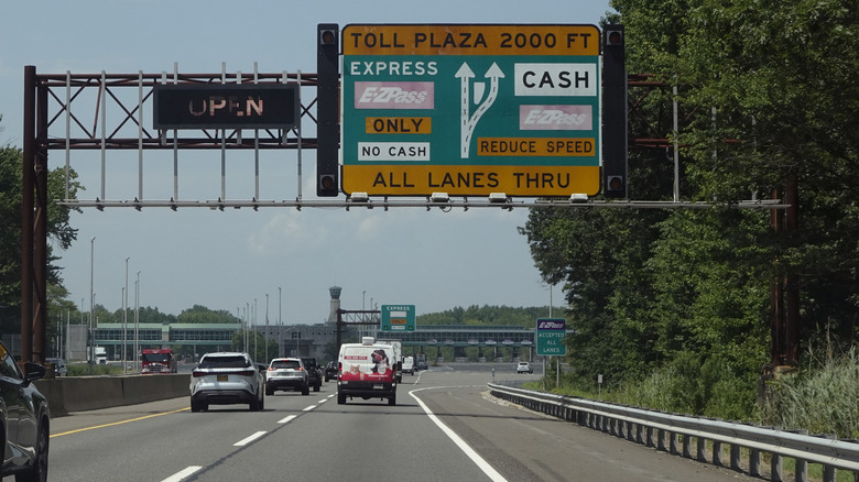 A busy road with a toll plaza sign overhead on a bright day