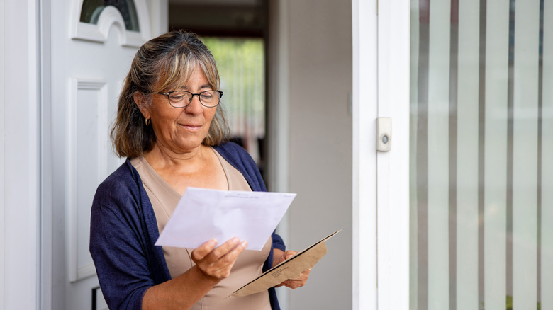 An older woman looks pleasantly surprised holding her mail