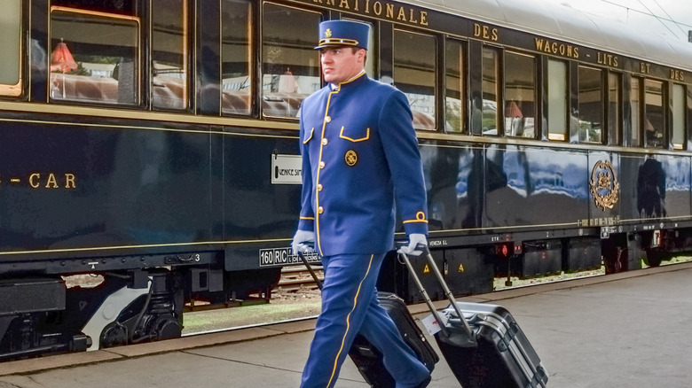 A porter carrying two bags through a European train station next to a train.