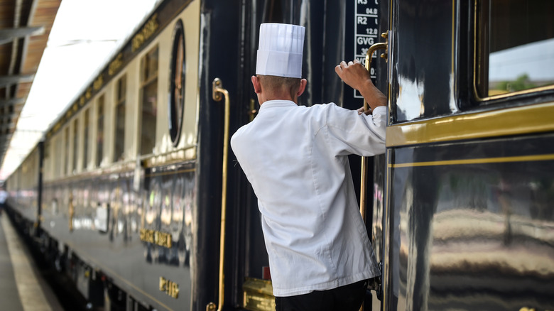 A chef hanging outsid the door of a luxury train.
