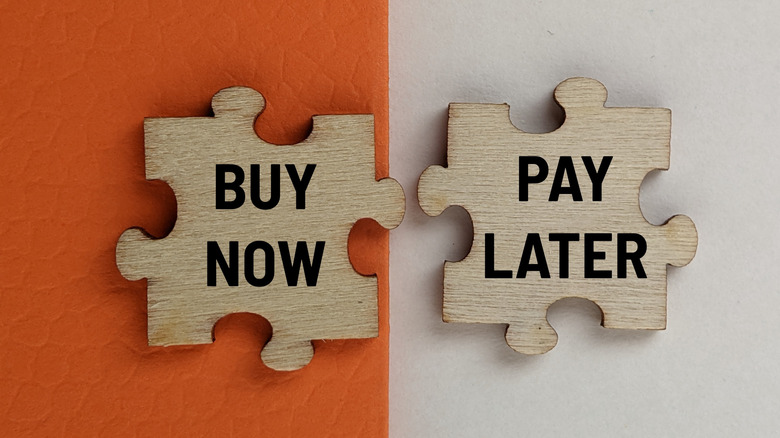 two wooden puzzle pieces, with one reading "buy now" and the other reading "pay later"