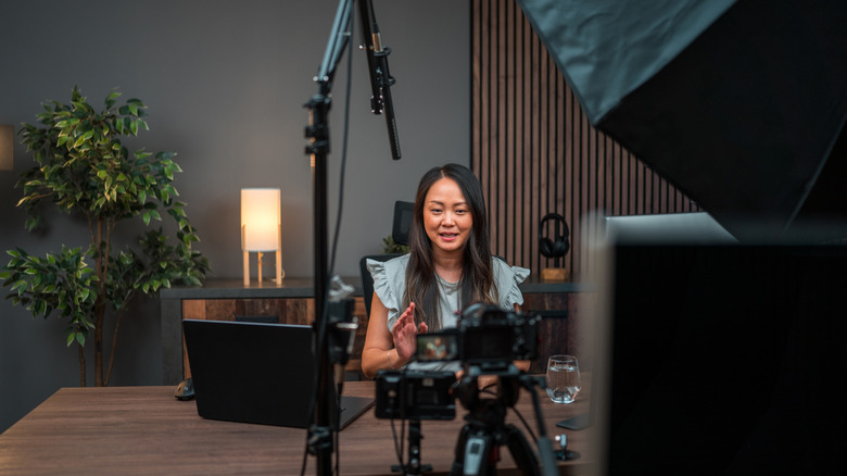 a content creator sitting at a table and talking with a camera pointed at her