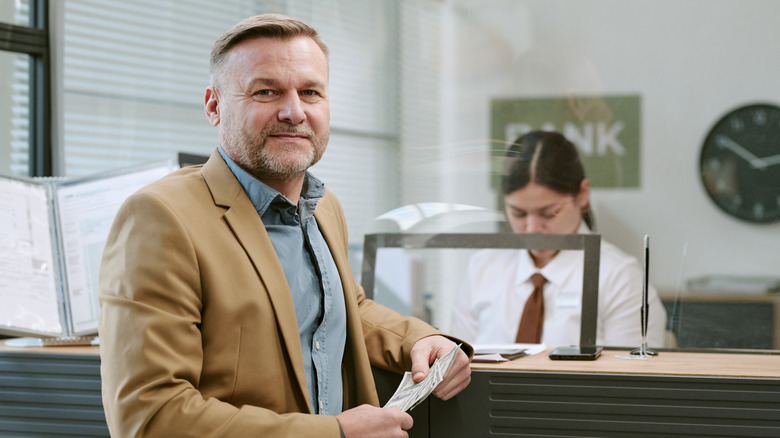 A man holding cash looking skeptical in front of a bank teller
