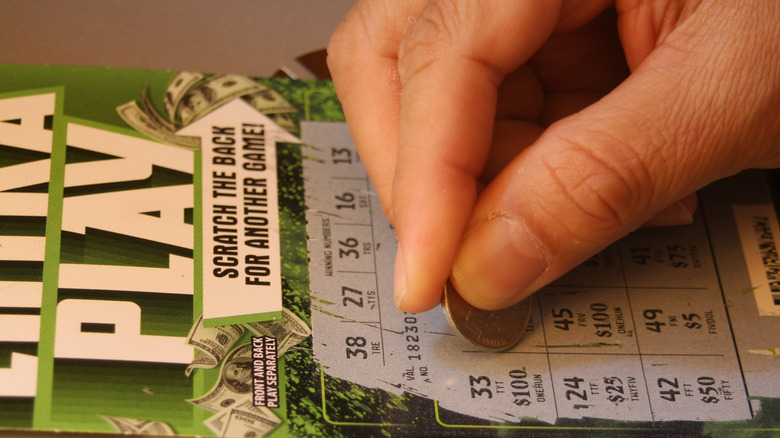 Hand scratching off a lottery ticket with a coin
