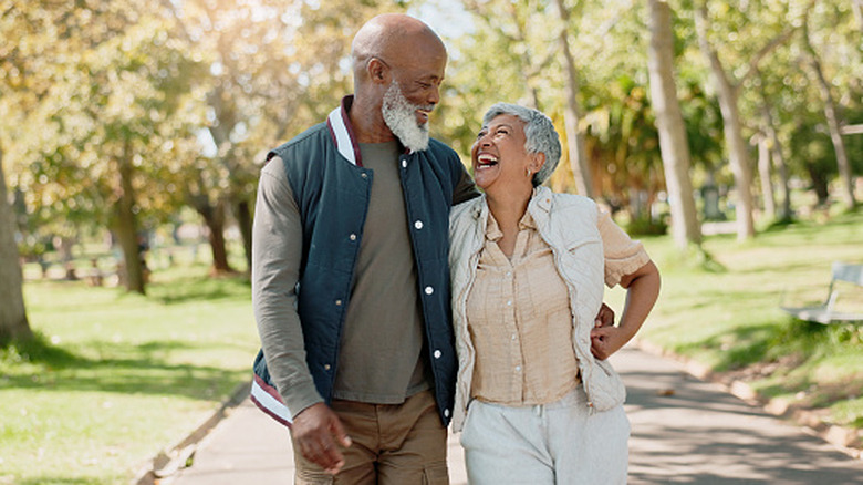 An older couple laughs as they walk through a park