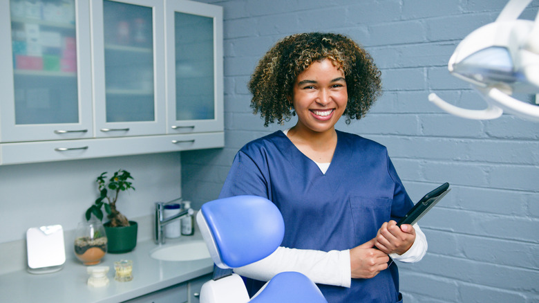 A happy women in a dental room holding a tablet.