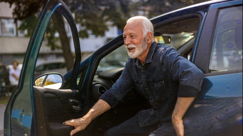An older man smiling as he steps out of a car with the driver's door open