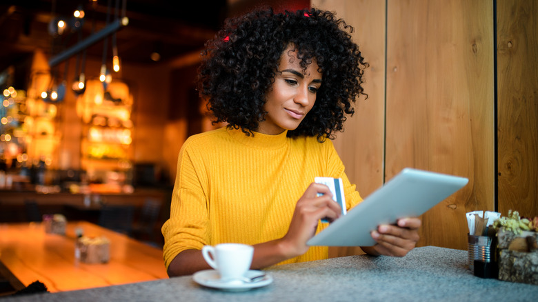 Woman sitting in café holding iPad and bank card with a coffee in front of her