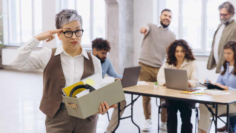 A middle-aged woman leaving her office with her possessions in a box
