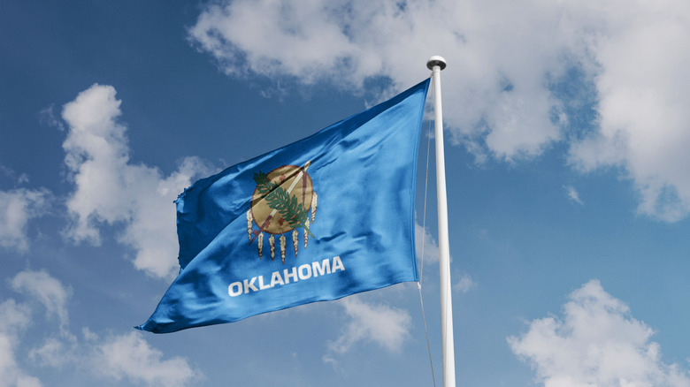 Oklahoma state flag waving against a blue sky.