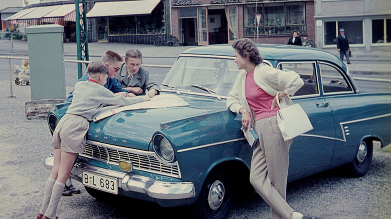 An old photo of a group of travelers looking over a map on the hood of a vintage car