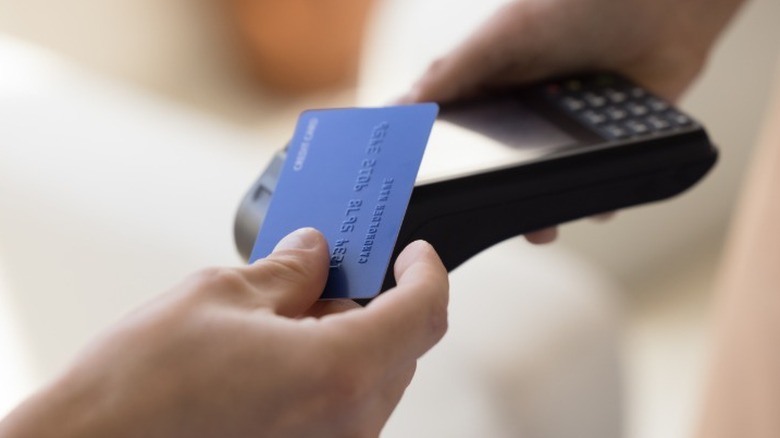 A person tapping a blue credit card on a handheld payment scanner.