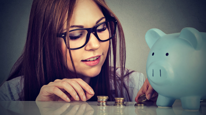 Young woman counting coins next to piggy bank