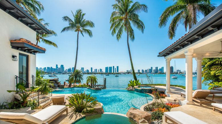 A luxury home's swimming pool on the water with Miami skyline in the background.