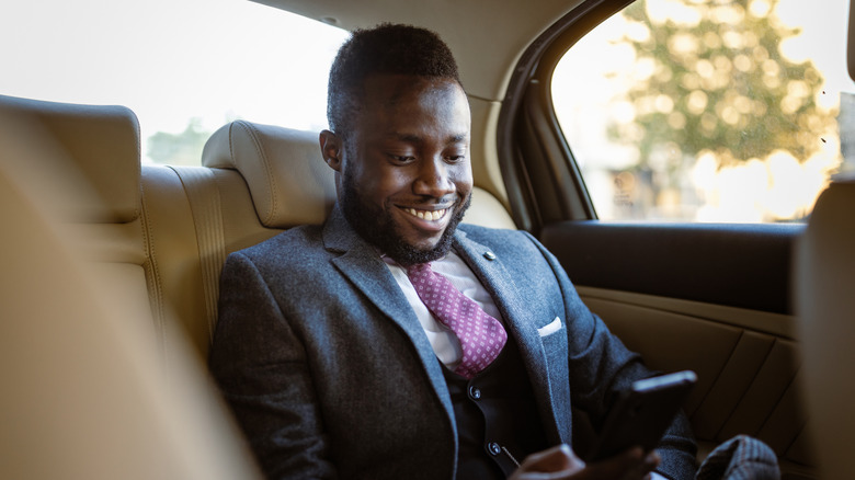 A weathy young man in a suit texting in the back seat of a limousine