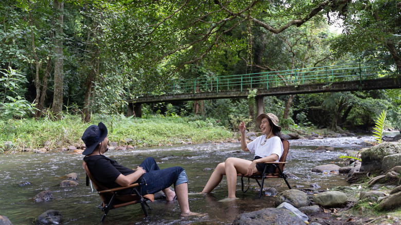 A couple sitting in a river under canopy of trees.