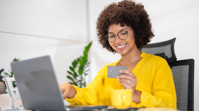 A smiling young woman holds a credit card while working at her computer