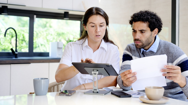 A couple looking at paperwork and a tablet over coffee in kitchen