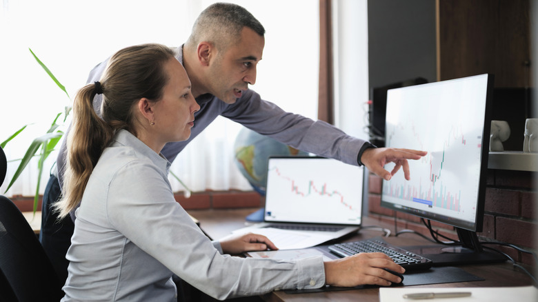 Man and woman studying investment charts on a computer screen