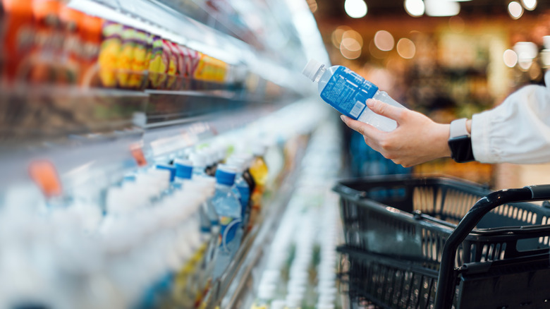 Close up of a person with shopping cart shopping for a bottle of healthy beverage from refrigerated shelves in a supermarket.